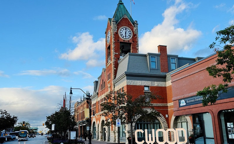 A red-brick clock tower stands by shops and a large CWOOD sign—why Collingwood?.