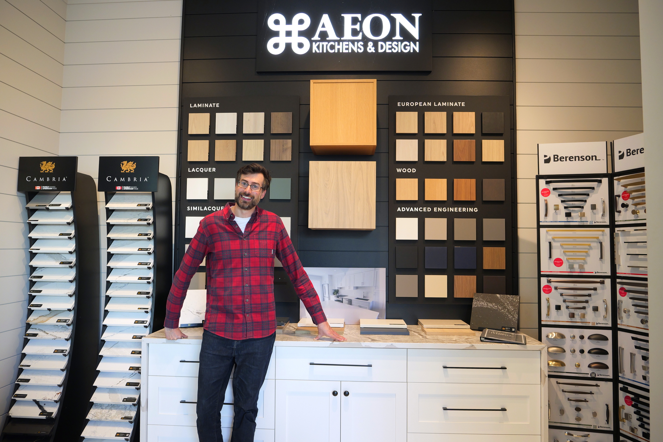 Man in a red plaid shirt stands in front of a kitchen design sample display at AEON Kitchens & Design.