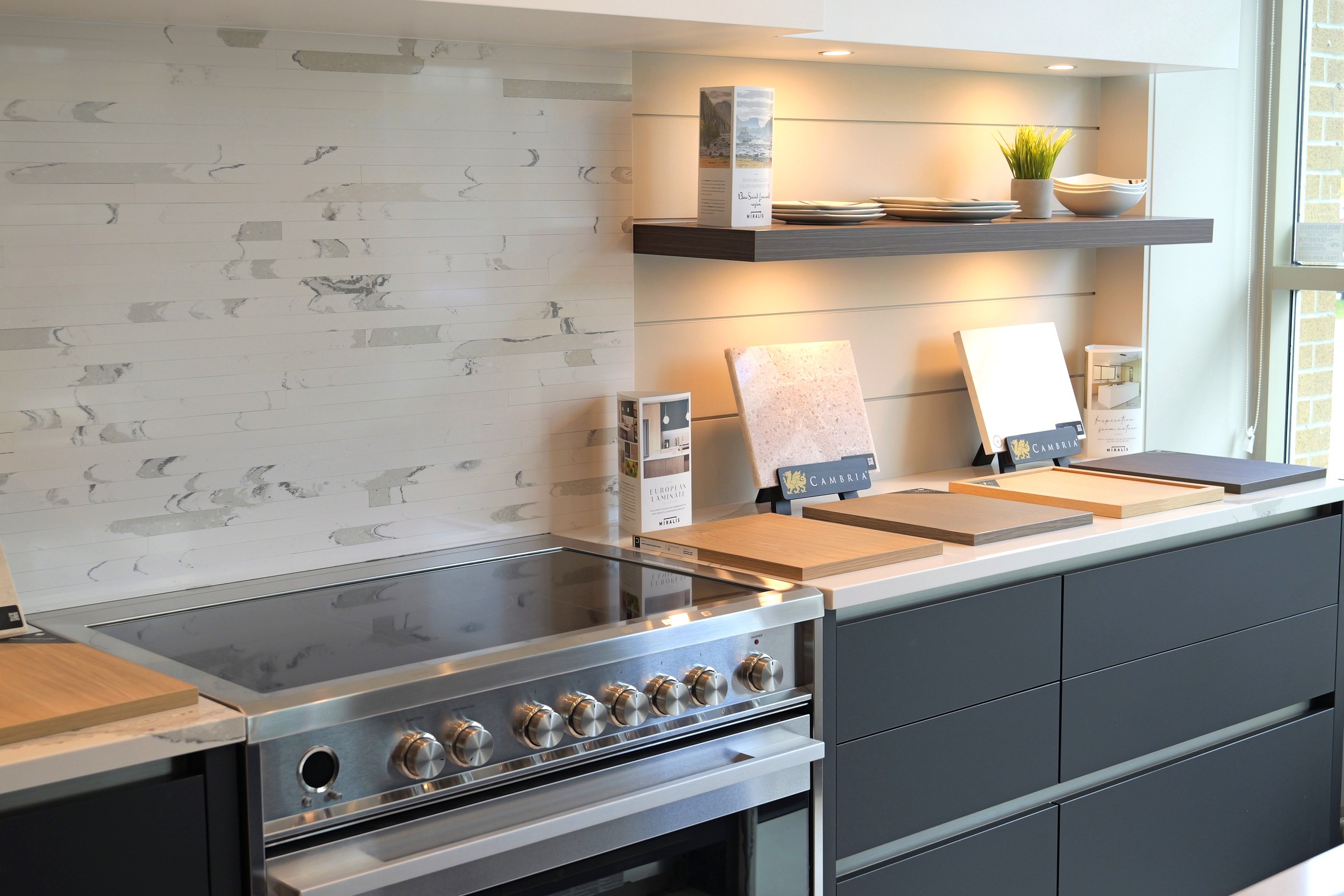 Modern kitchen with a stainless steel stove, samples on the counter, and floating shelves.