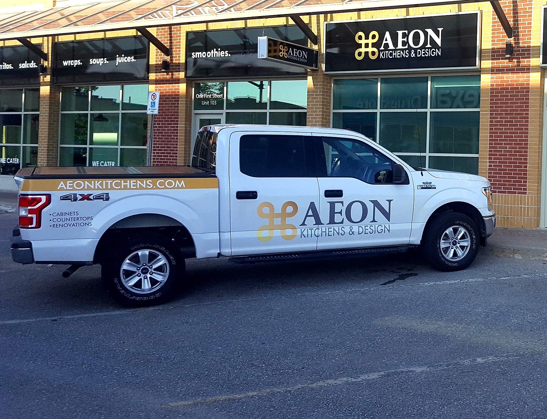 White pickup truck with AEON Kitchens & Design branding parked outside the business storefront.